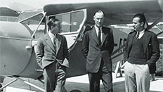 Three men standing by an old light aircraft