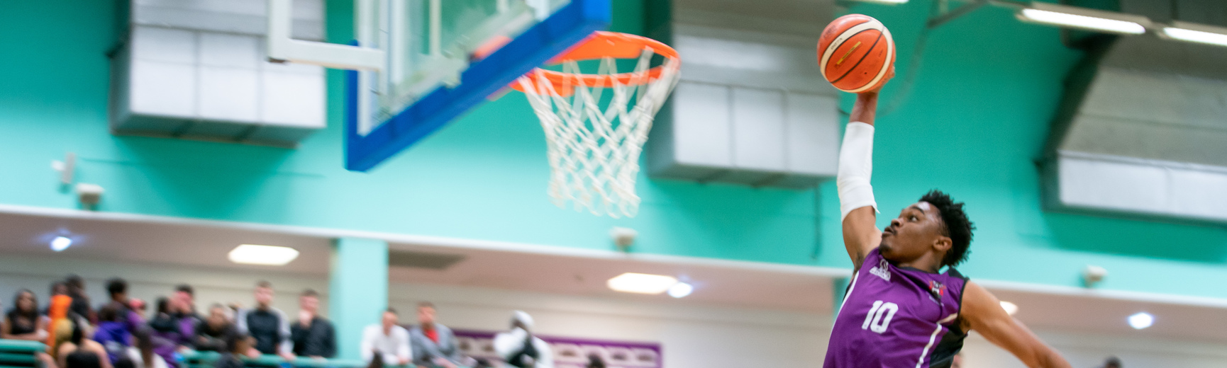 a male student about to dunk a basketball through a hoop in a competitive game