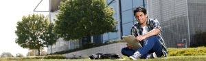 male student sits on grass outside LRC studying on laptop