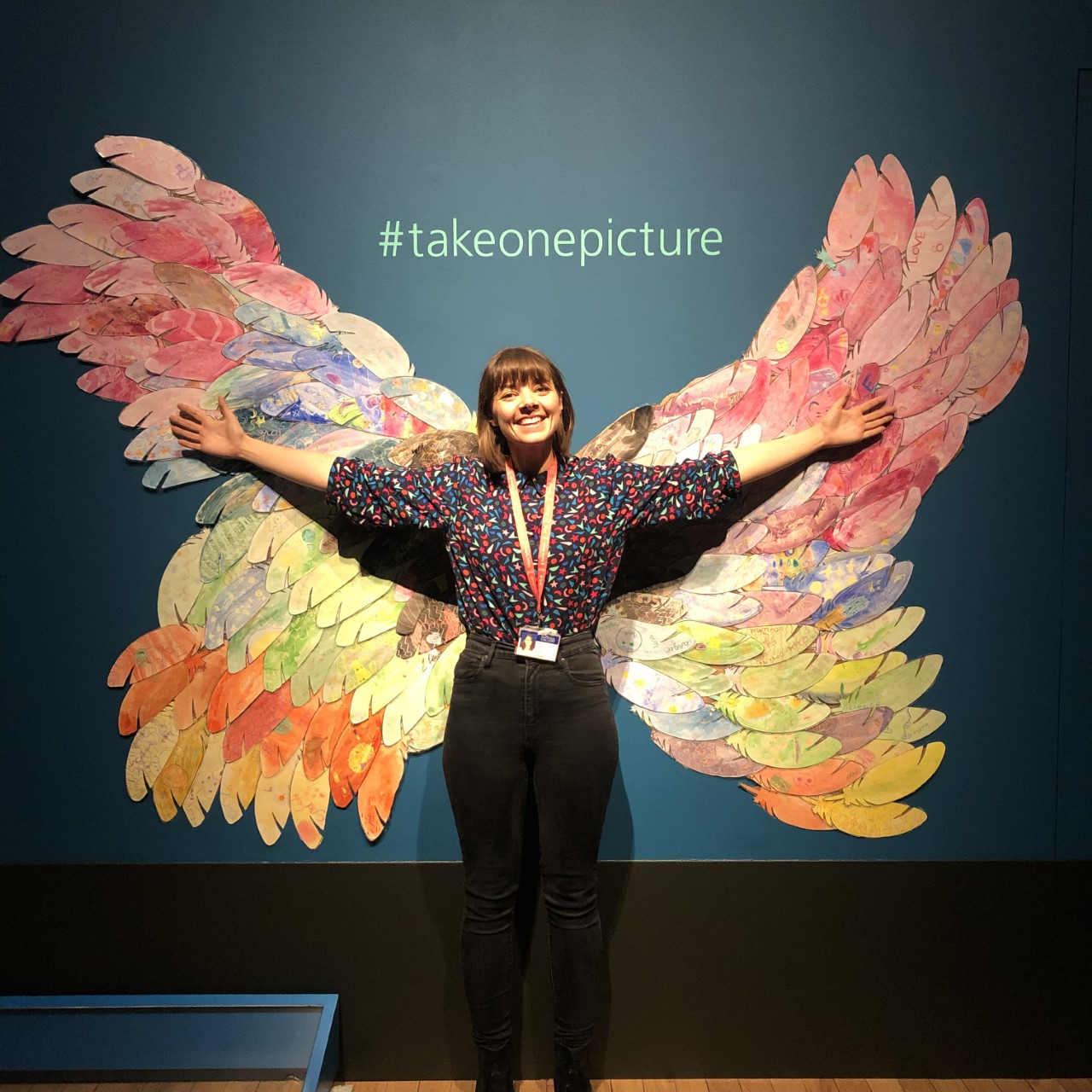 A portrait of Nicola standing against a wall with a bird's wing