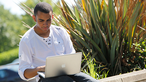 a student sits on the grass with his laptop