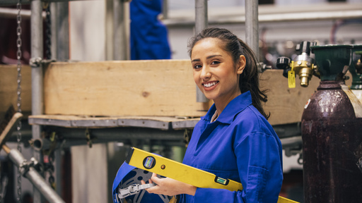 Female engineering in a workshop holding a helmet and level
