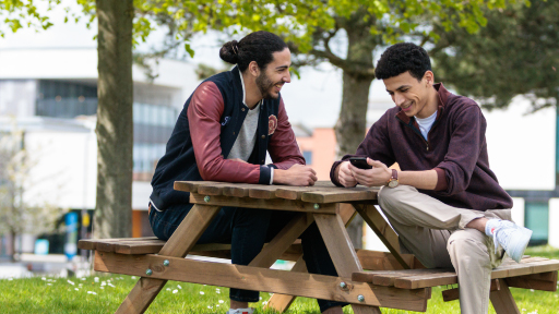 Two students sitting on a bench looking at a phone