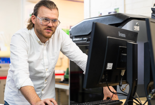 Male student standing working on a computer 