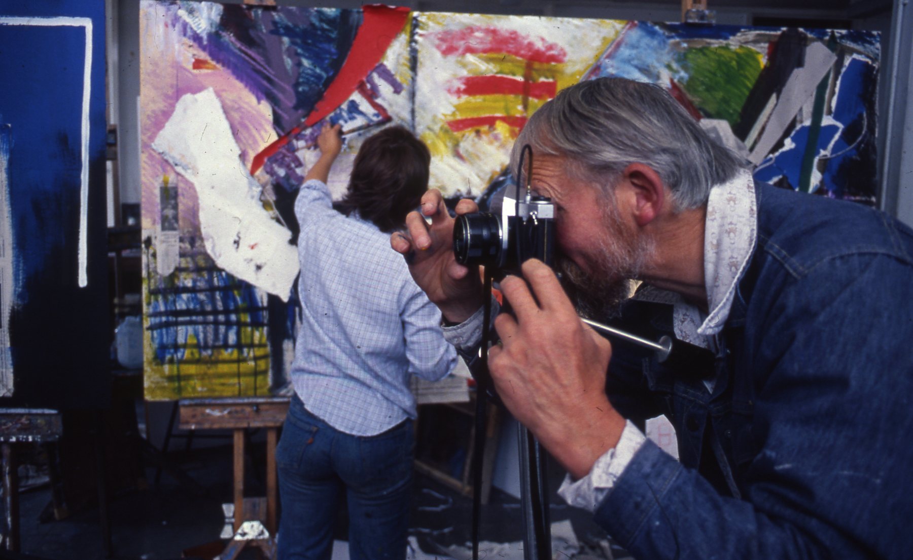 Two blurred figures painting a large canvas