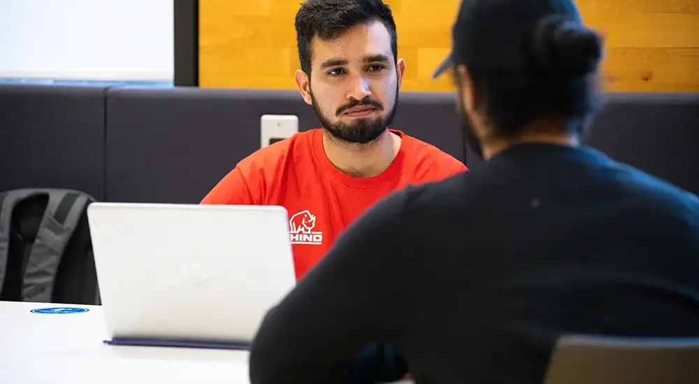 A person in a red top sitting in front of a laptop talking
