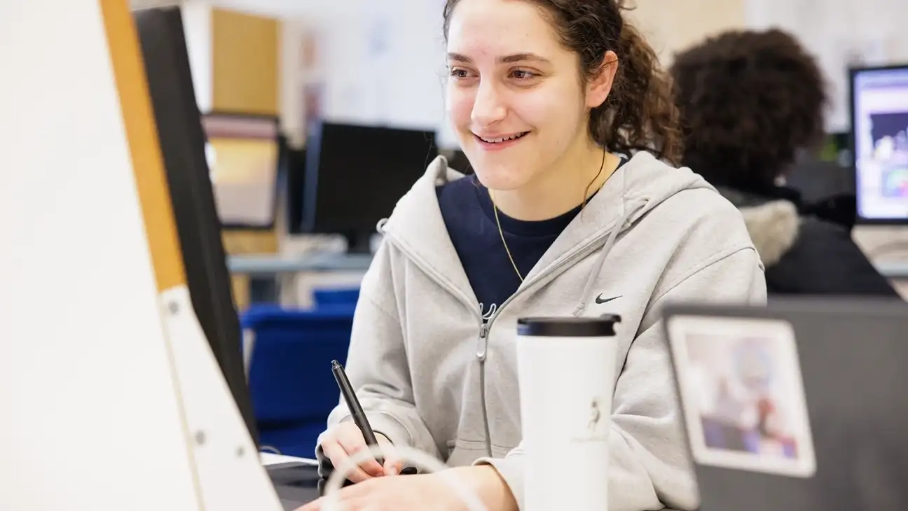A student working on a desktop computer smiling