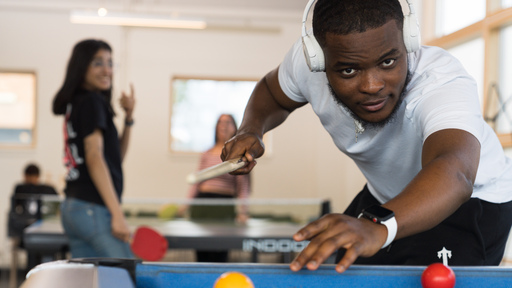 Black male student playing pool while friends laugh in background