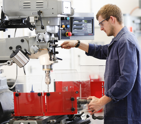 Student in overalls using pillar drills