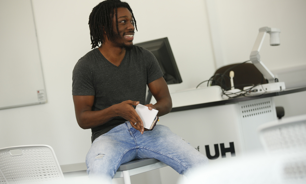 a male student sitting in a classroom, engaged in conversation and smiling 