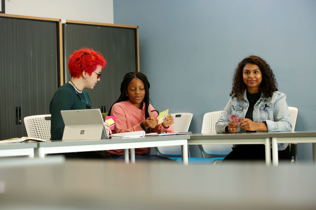 three students studying language in class. smiling and focused. 