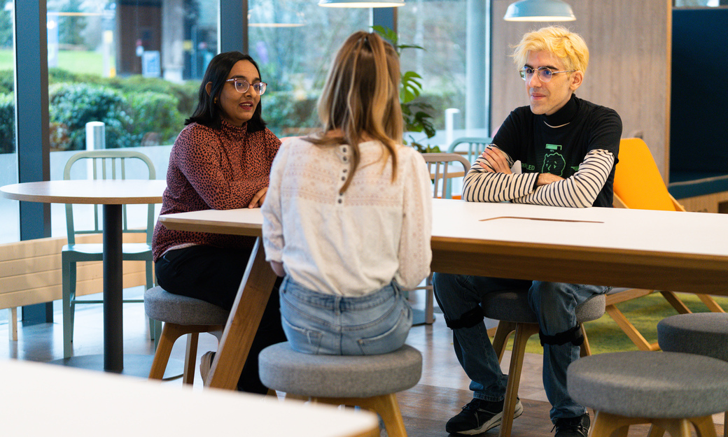 three students sitting at a table in the enterprise hub. they look like they are in deep discussion. 