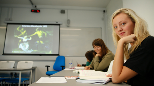Student looking at the camera, book on the table and projector on in the background 