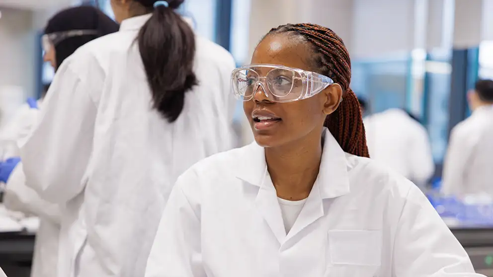 Student in a lab wearing a lab coat and safety goggles