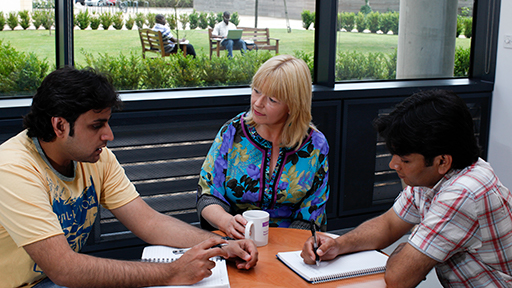 A teacher and two students sit around a table talking