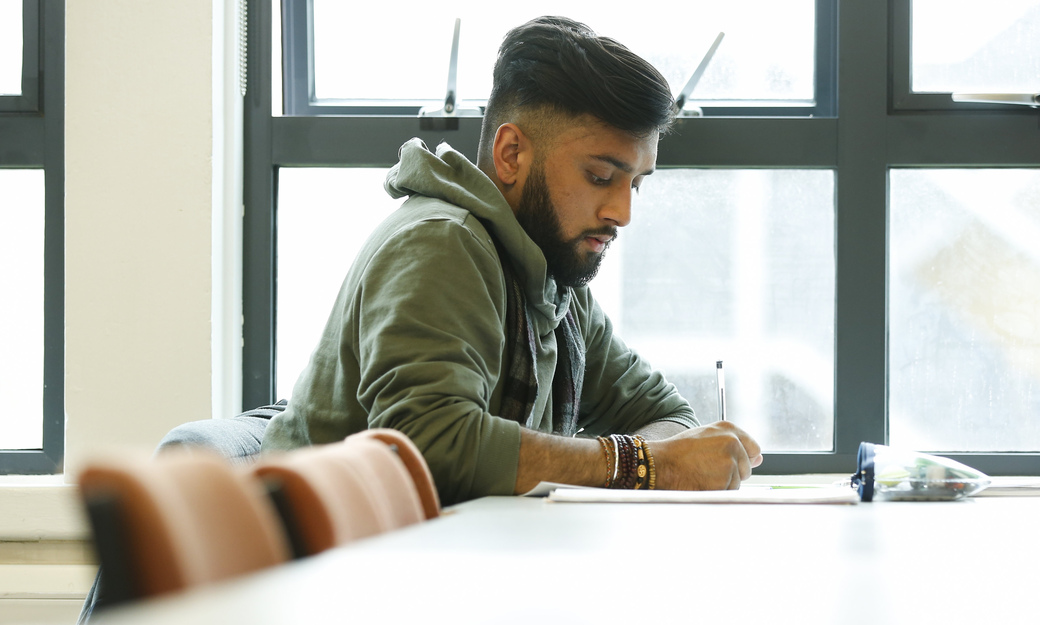 a male student focusing on writing notes in a lecture. 