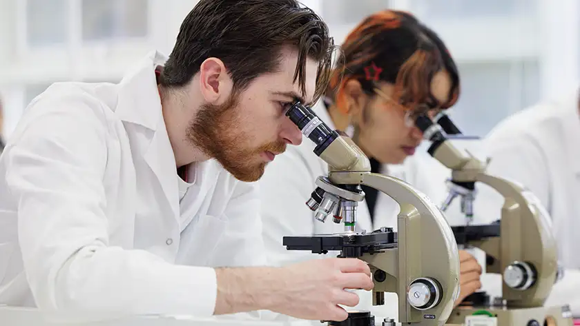 Two students in lab coats looking at microscopes