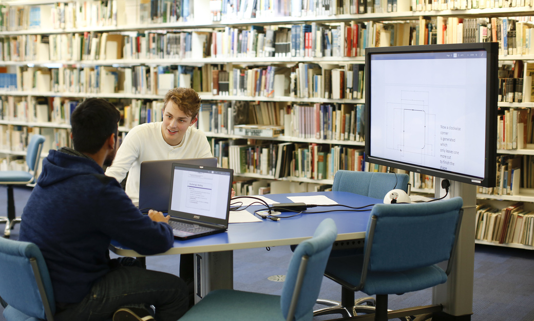 two students collaborating on a project using the group desks and screens in the library