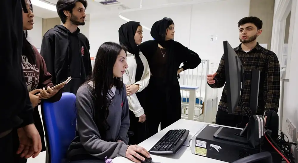 A group of students standing taling with one student in front of a computer