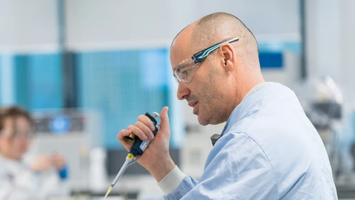 A person in a lab coat and glasses holding a pipet