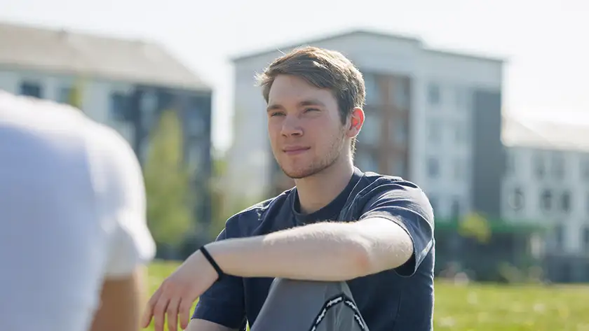 A student sitting on grass in the on a sunny day outside the University