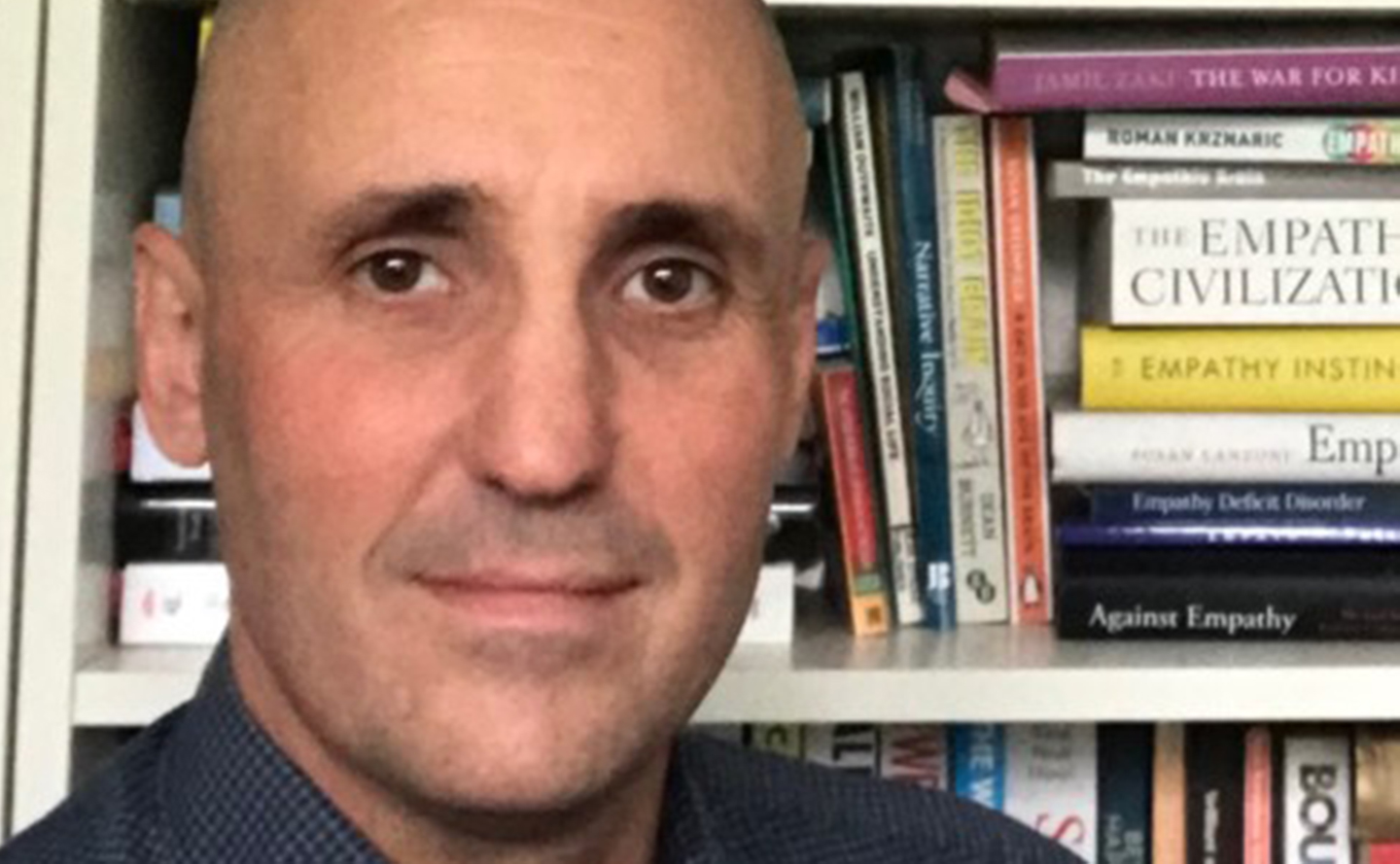 Peter Sear stands by a bookcase looking to camera