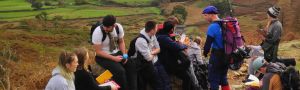 A group of students sit on rocks in the countryside as they make notes