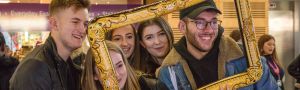 a group of students smile behind a blow up photo frame