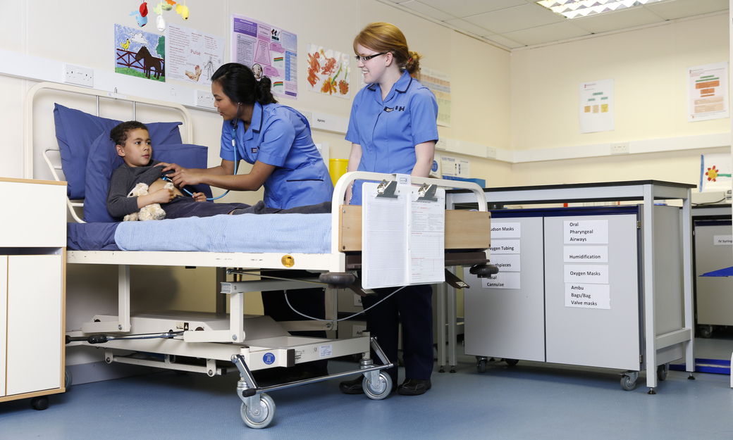 two student nurses comforting a child in a ward bed