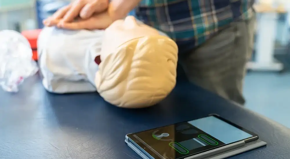 A student performing CPR on a dummy with a phone counting rhythm