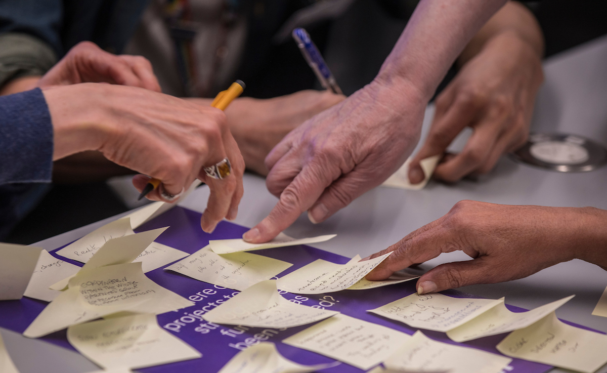 Hands pointing to a purple board covered with Post Its